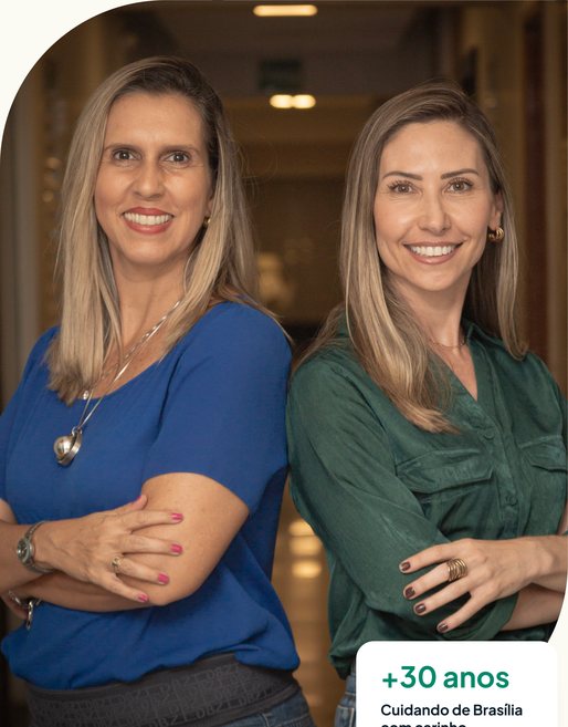 Duas profissionais da Clínica Cliff sorrindo, de braços cruzados, no corredor da clínica